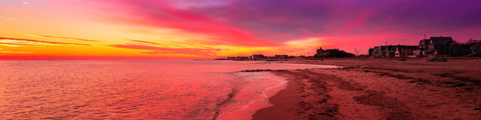 Vibrant saturated pink and blue seascape at sunrise. Curved beach, gentle waves, dramatic clouds over the coastal village. Stunning red twilight landscape over Falmouth Height Beach on Cape Cod.