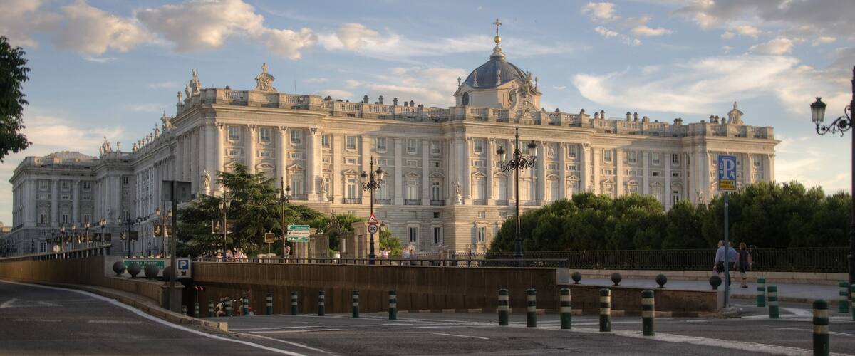 A large, ornate building with classical architecture, including columns and statues, under a partly cloudy sky.