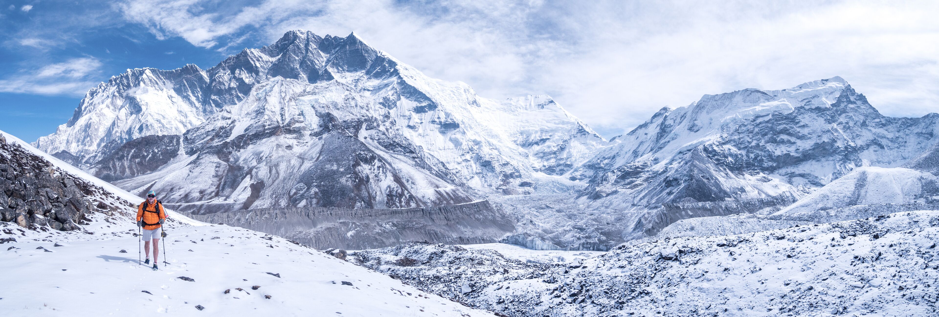 A snow-covered mountain range with a hiker in an orange jacket.