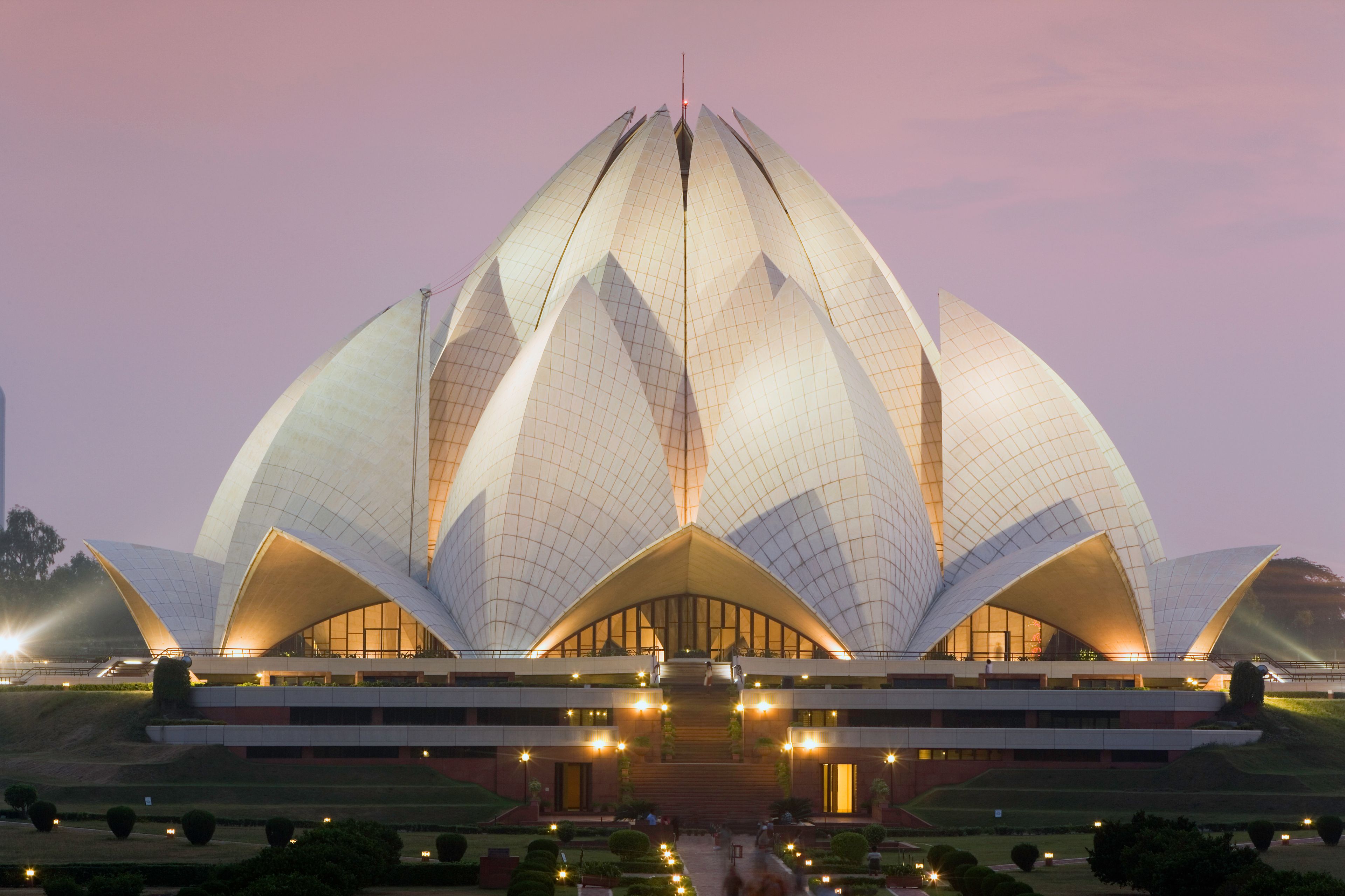 A large, white, lotus-shaped building with a grid-like pattern on its surface, surrounded by a landscaped area with pathways and trees.