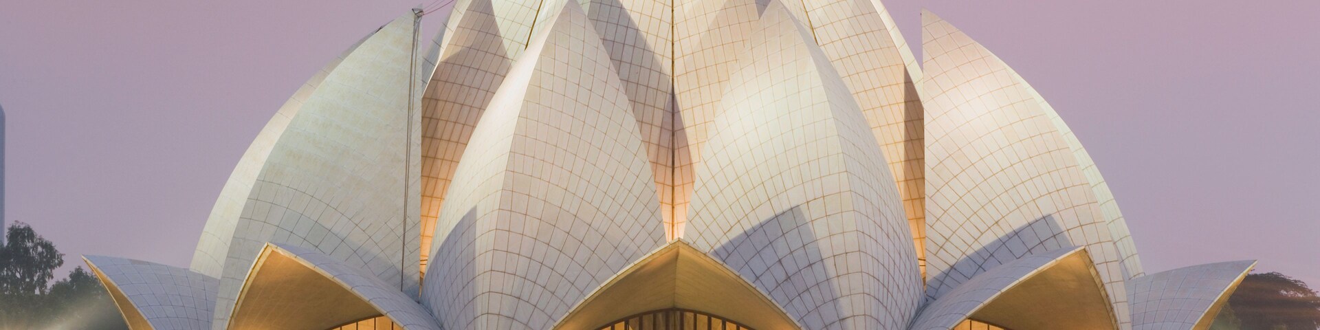 Um edifício grande e branco em forma de lótus, com um padrão em grade na superfície, rodeado por uma área ajardinada com caminhos e árvores.