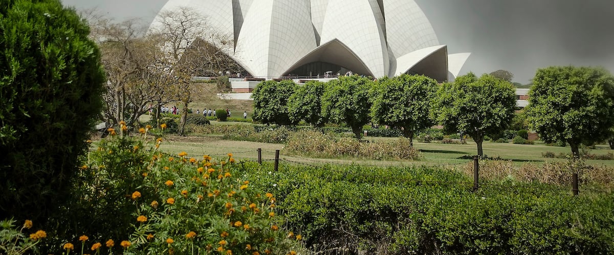 A large white building with a unique architectural design, surrounded by greenery and under a cloudy sky.