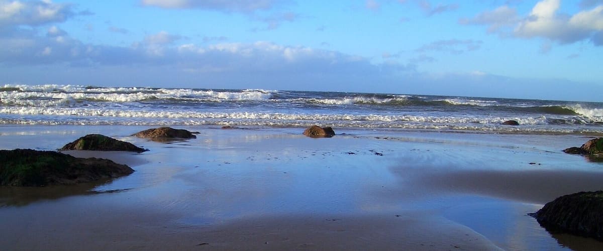 A beach with waves crashing onto the shore and rocks scattered along the sand.