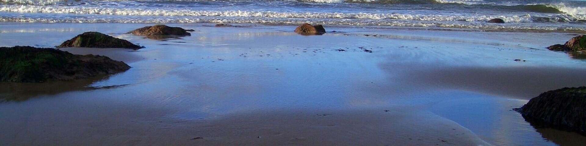 A beach with waves crashing onto the shore and rocks scattered along the sand.