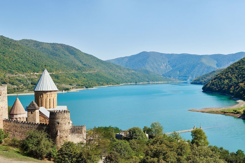 Un château historique dominant un lac turquoise, lui-même entouré de collines verdoyantes.