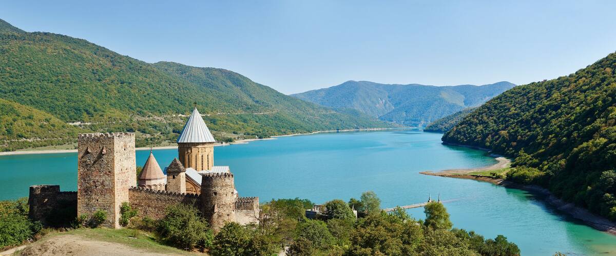 A historic castle overlooking a turquoise lake surrounded by lush green hills.