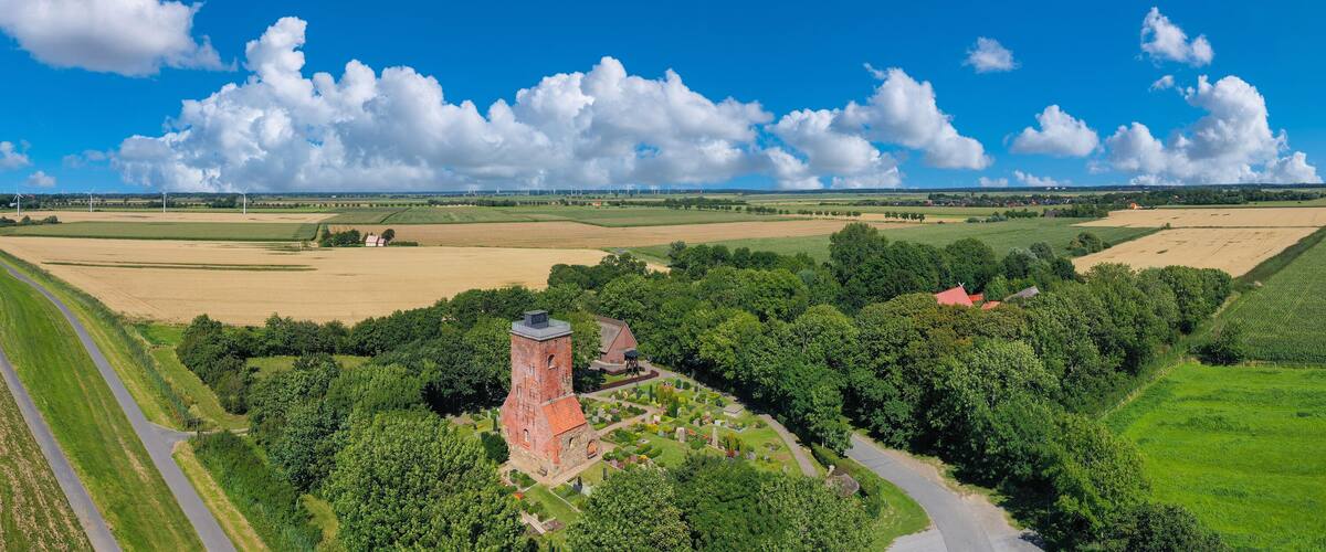 A coastal landscape with wind turbines, a church, and a cemetery.