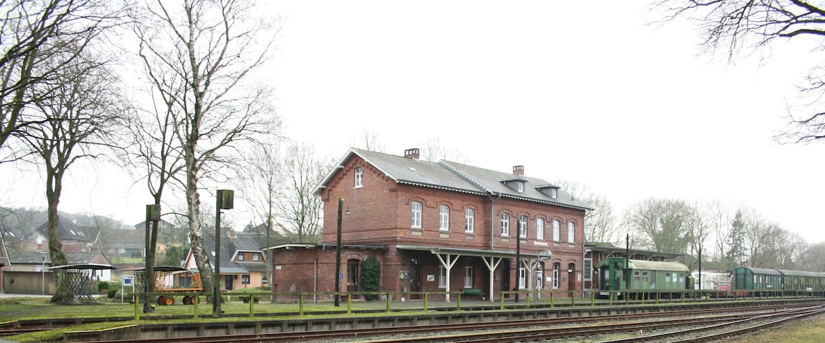 A brick building with a green train on the tracks.