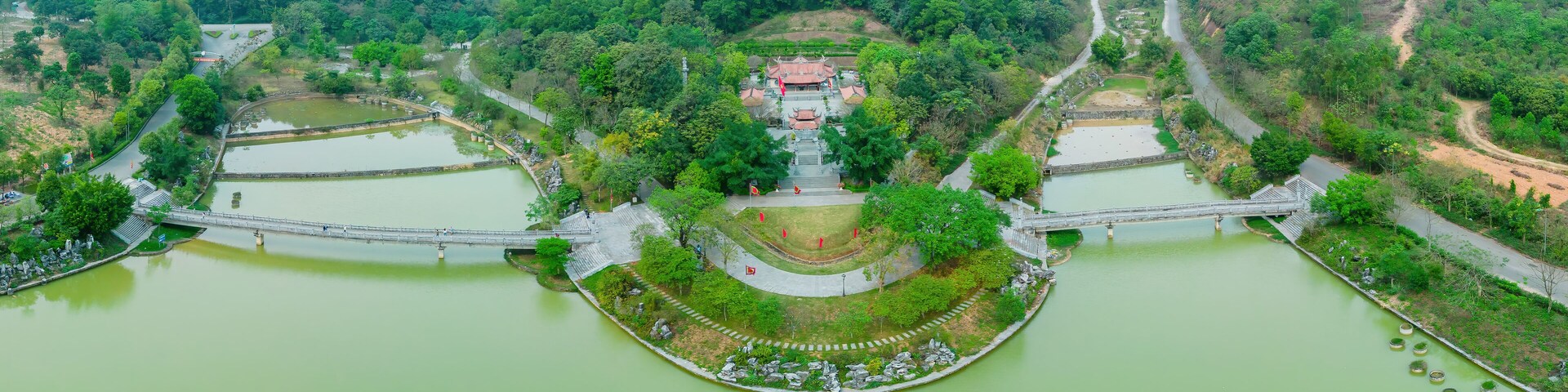 A riverside temple complex with a central pagoda, surrounded by lush greenery and connected by bridges.