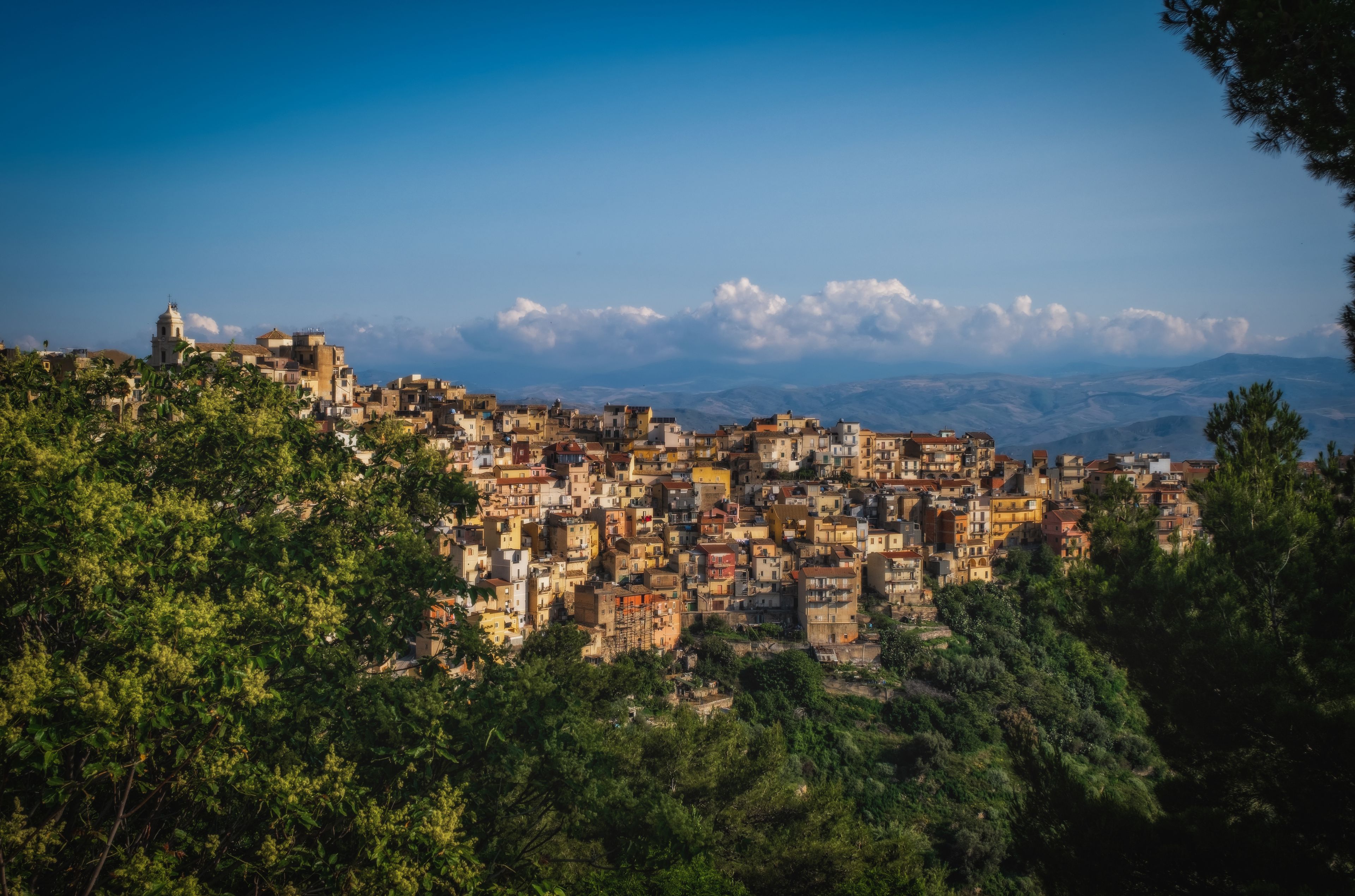 A densely packed hillside town with historic architecture, surrounded by lush greenery and mountains in the background.