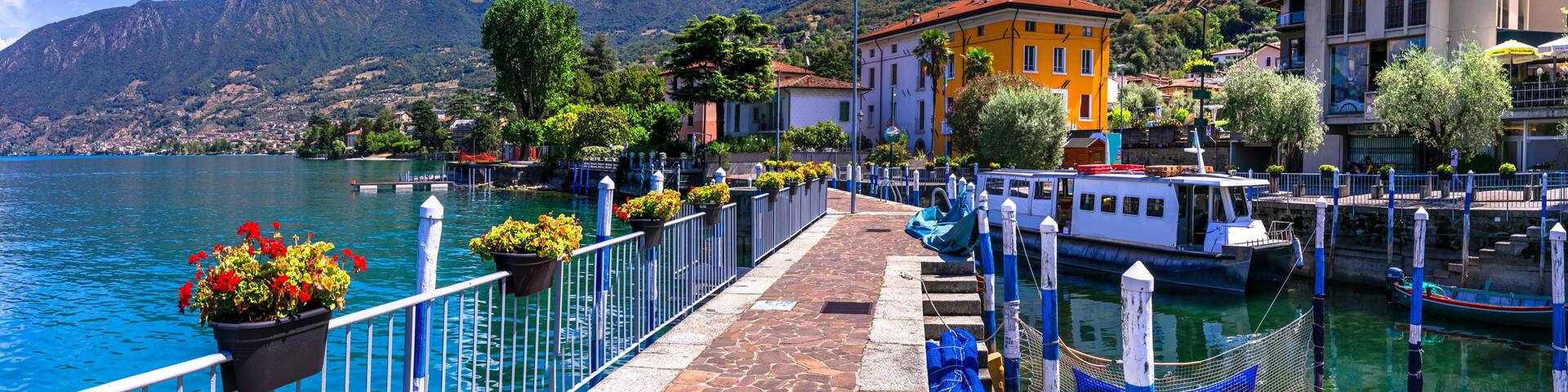 A waterfront promenade with a row of colorful buildings, a gondola, and a mountain backdrop.