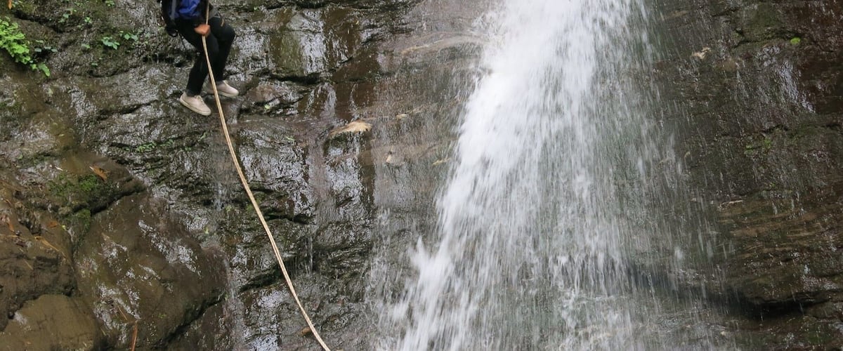 A hiker on a rocky cliff with a waterfall.