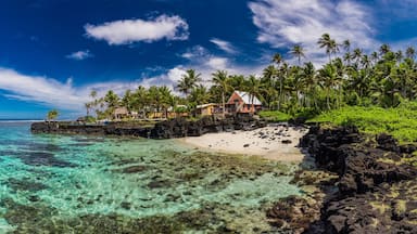 Uma praia tropical com águas turquesa cristalinas, um litoral rochoso e um resort com palmeiras.