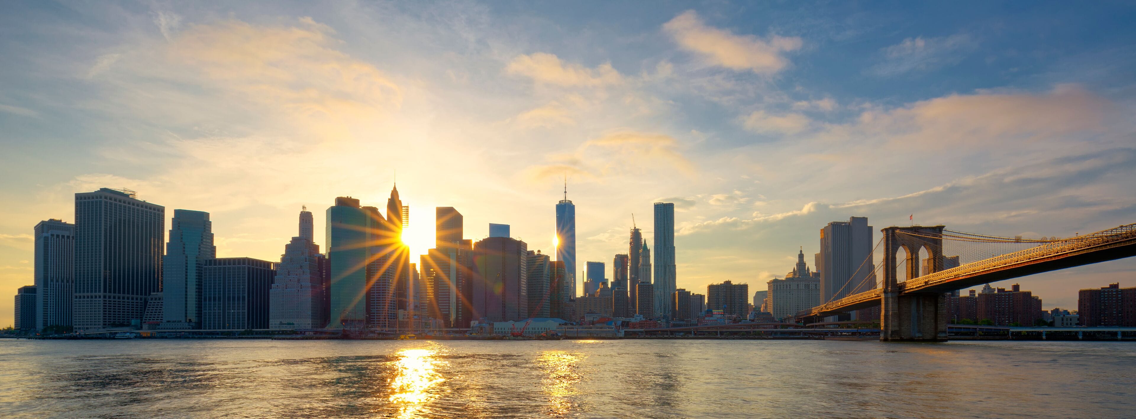 A city skyline with a prominent bridge and the sun setting behind the buildings.