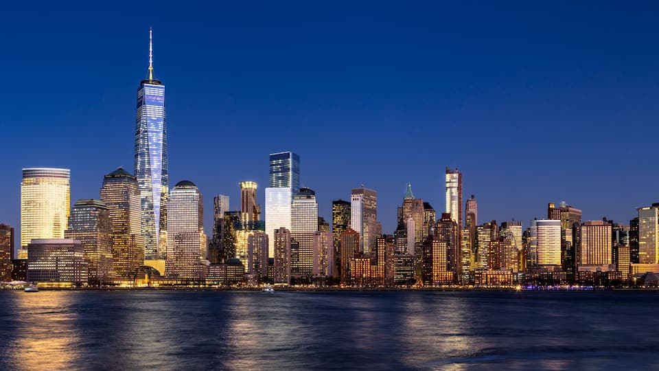 Linha do horizonte urbana com um arranha-céu imponente, vários outros edifícios altos e um corpo d'água em primeiro plano.