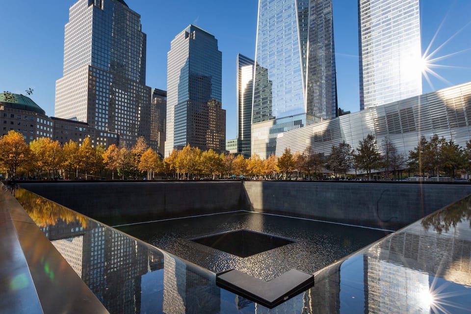 A modern cityscape with tall skyscrapers and a reflective water feature in the foreground.