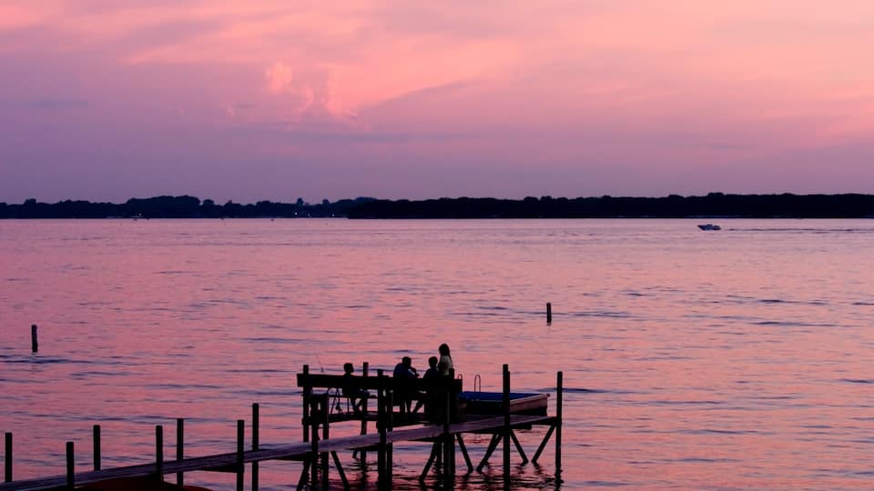 A sunset over a calm lake with a dock and people sitting on it.