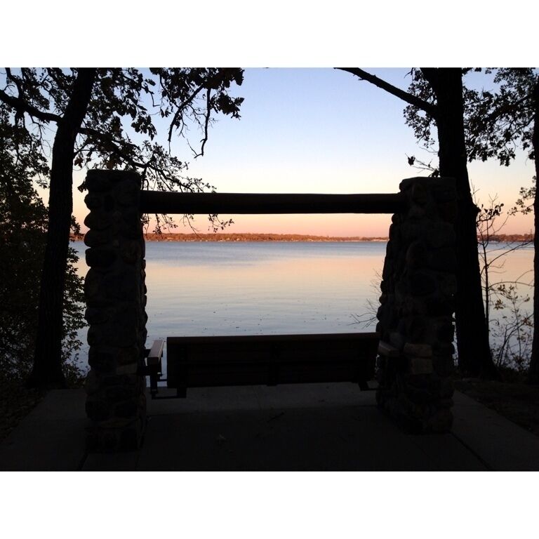 A stone bench overlooking a calm body of water during sunset.