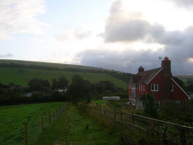 A red house in a rural setting with green fields and a cloudy sky.