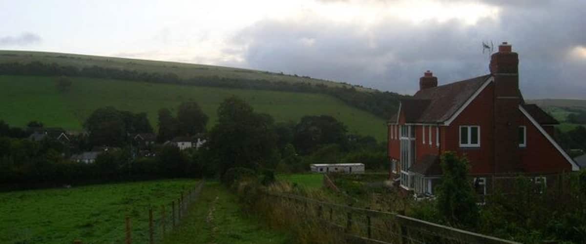 A red house in a rural setting with green fields and a cloudy sky.