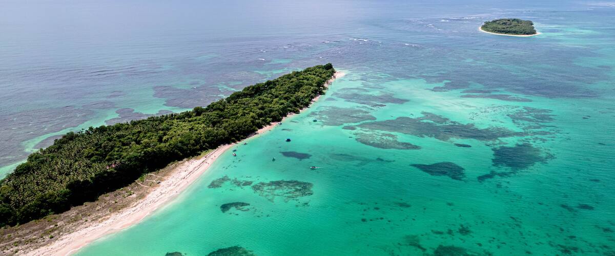 An aerial view of a tropical island with a long, narrow beach and clear turquoise waters.