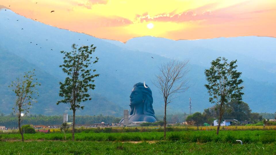 A large statue in a field with mountains in the background.