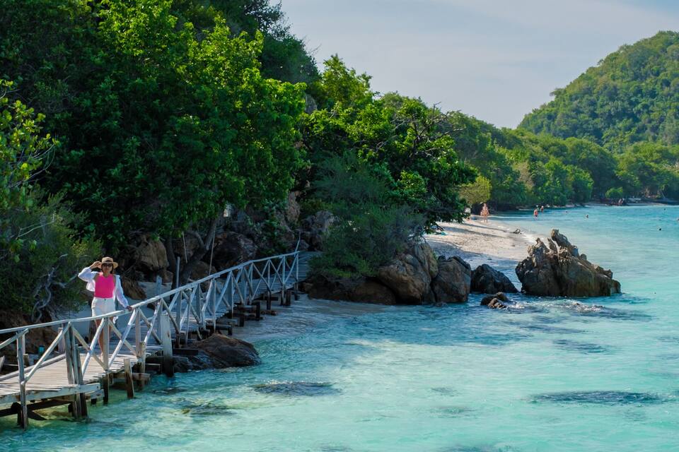 A wooden bridge over clear turquoise water, surrounded by lush greenery and rocky outcrops.