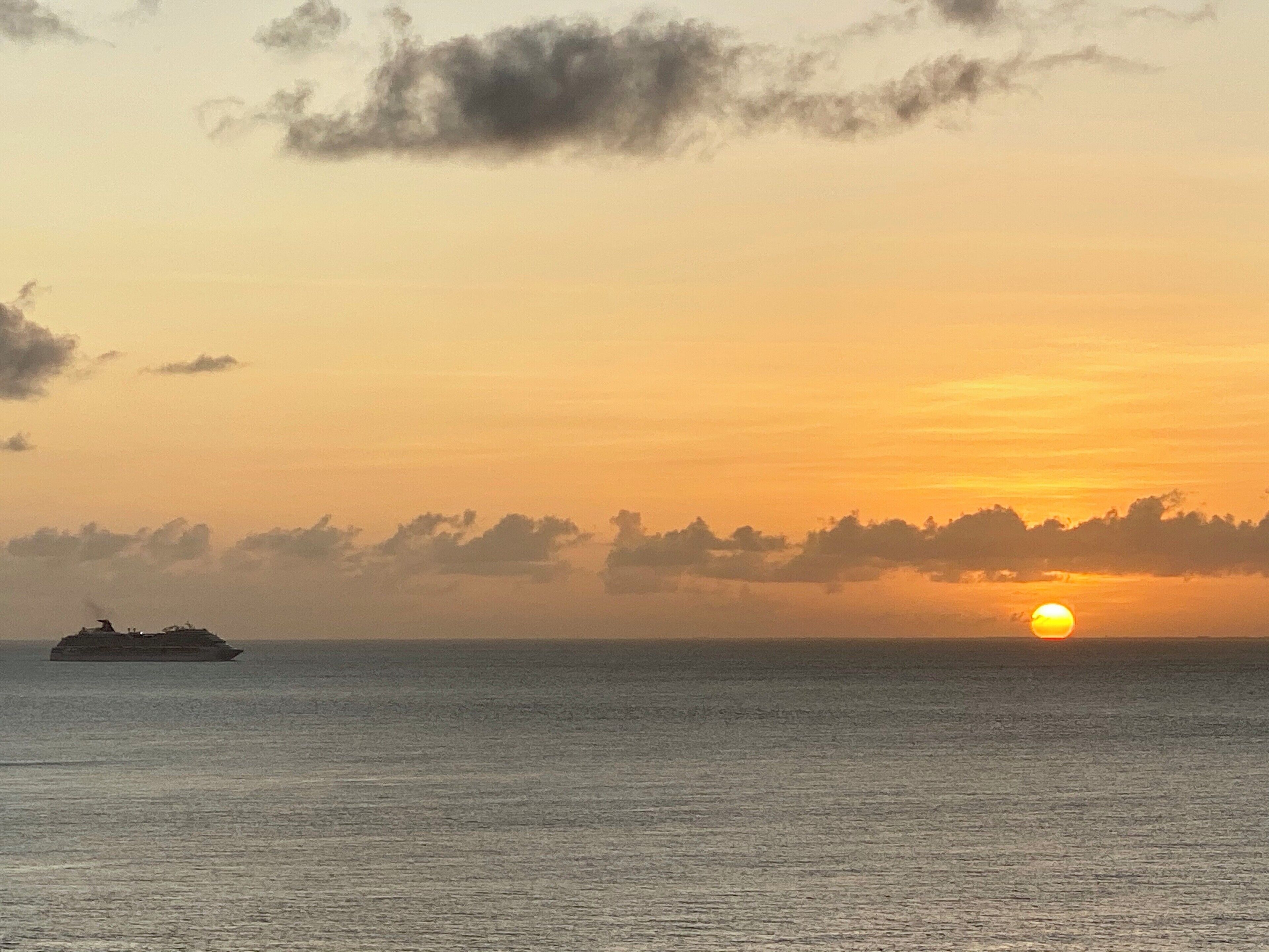 A sunset over a calm sea with a ship in the distance.