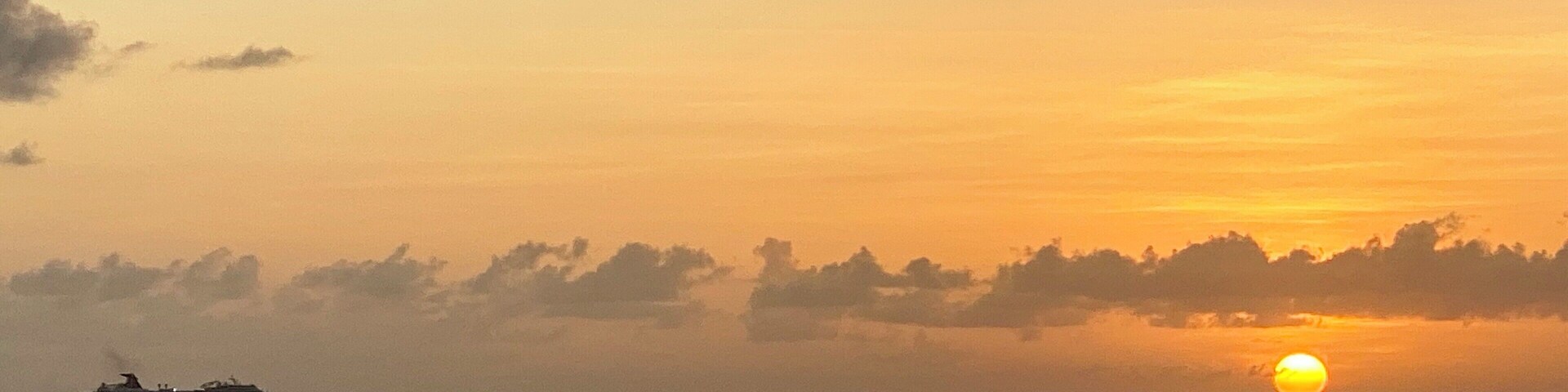 A sunset over a calm sea with a ship in the distance.
