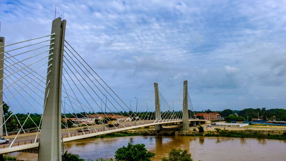 A cable-stayed bridge over a river with greenery and buildings in the background.