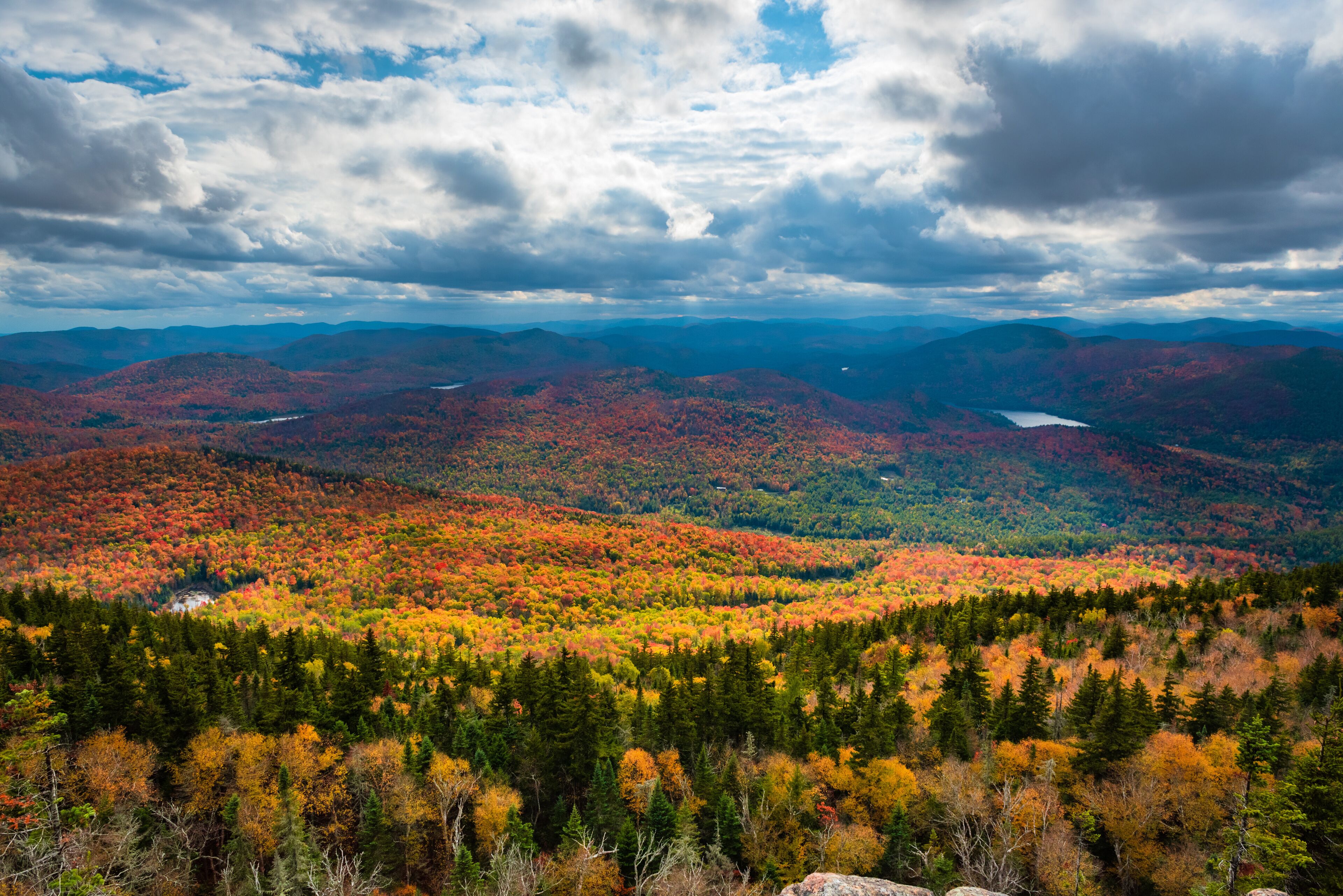 A mountainous landscape with autumn foliage, a lake, and a cloudy sky.