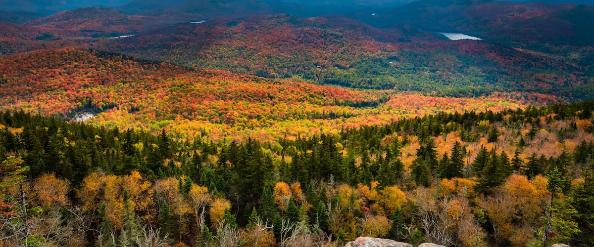 A mountainous landscape with autumn foliage, a lake, and a cloudy sky.