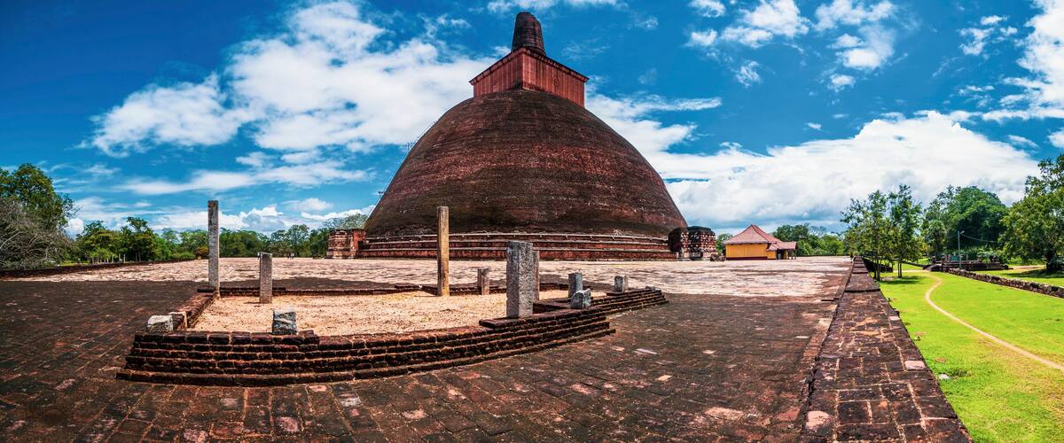 A large, domed structure with a brick exterior and a red roof, surrounded by a paved area and a grassy path.
