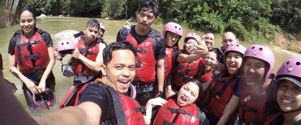 A group of people wearing life jackets and helmets by a river.