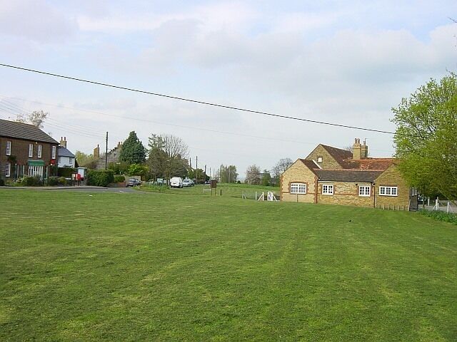 A grassy field with a stone building and a red car in the distance.