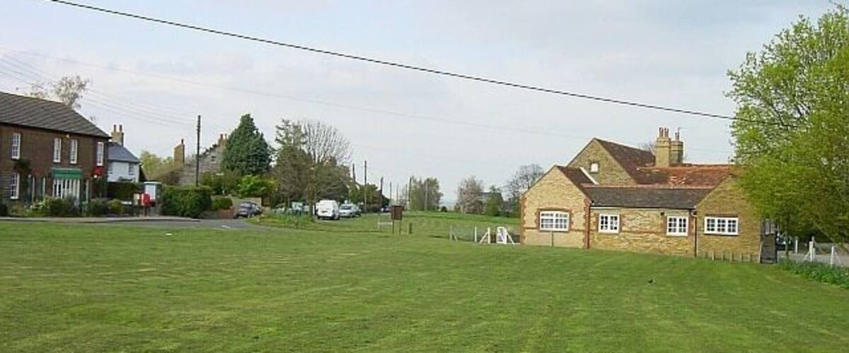 A grassy field with a stone building and a red car in the distance.