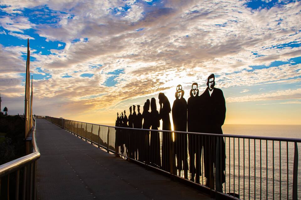 A boardwalk with people silhouetted against a sunset sky.