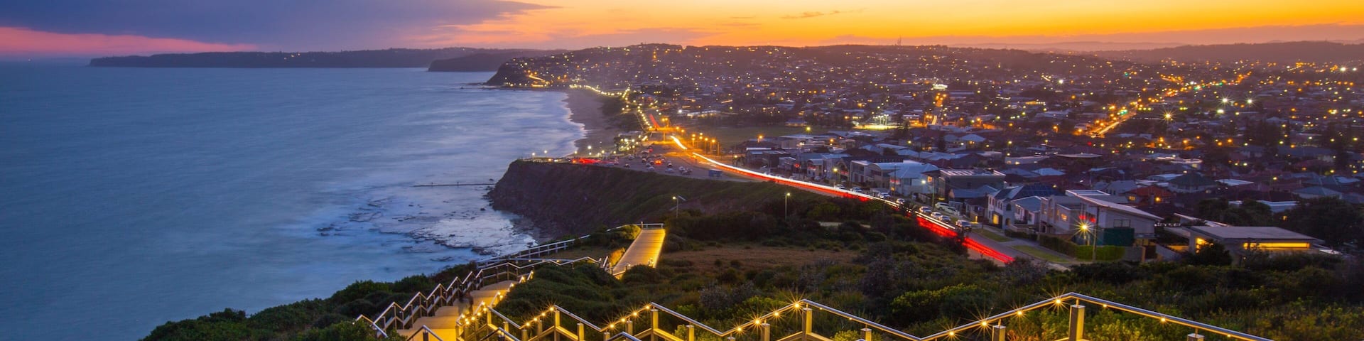 A coastal city at sunset with a prominent staircase leading down to the beach.