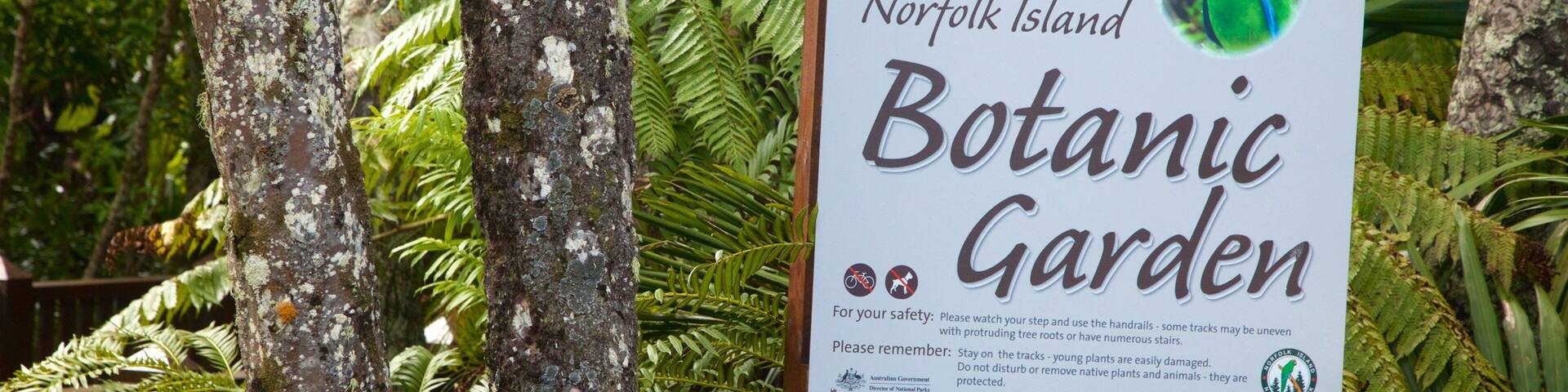 A sign welcoming visitors to Norfolk Island Botanic Garden, surrounded by trees and ferns.