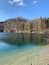 A clear lake with a rocky shore, surrounded by trees and a small cabin.