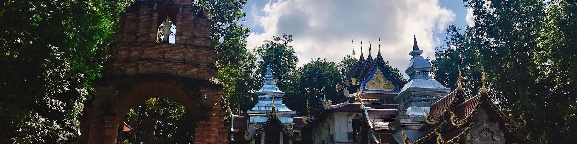 A temple complex with a prominent brick archway, traditional Thai architecture, and a clear blue sky.