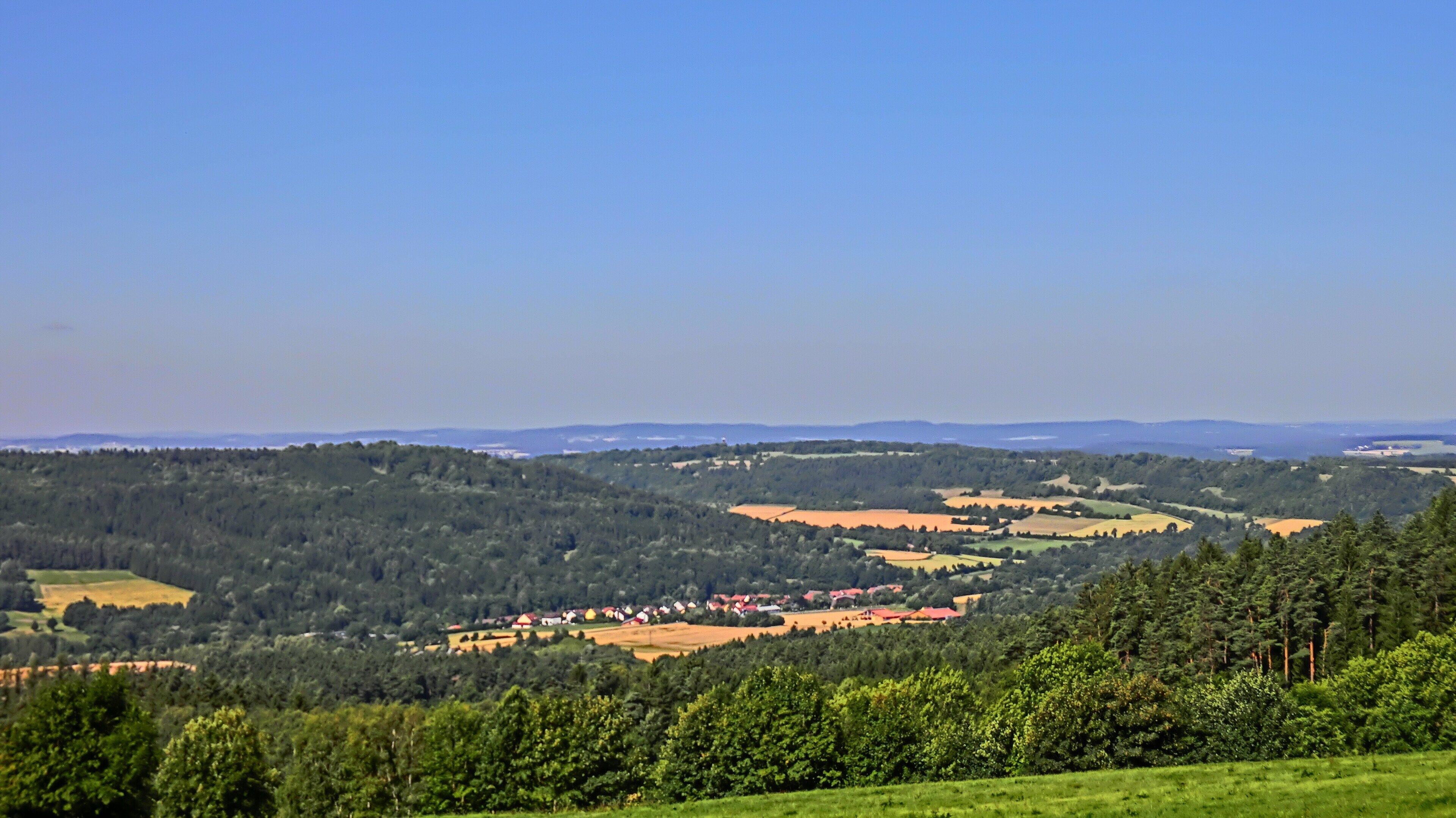 A rural landscape with rolling hills, a small village, and dense forests.