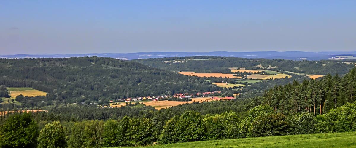 A rural landscape with rolling hills, a small village, and dense forests.