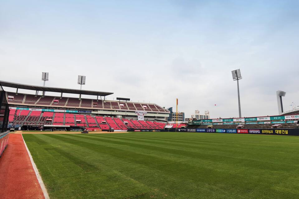 Een groot, leeg stadion met rode zitplaatsen en groen gras.