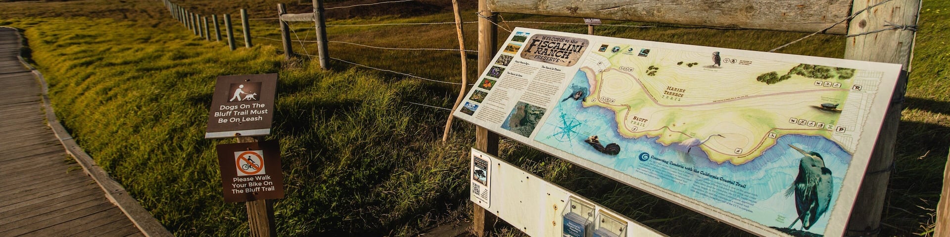A wooden boardwalk leading to a large informational sign about the Bluff Trail.