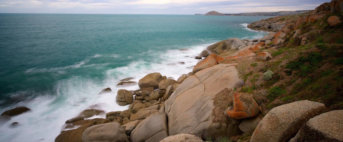 A coastal landscape with large boulders, a rocky shoreline, and a distant mountain.
