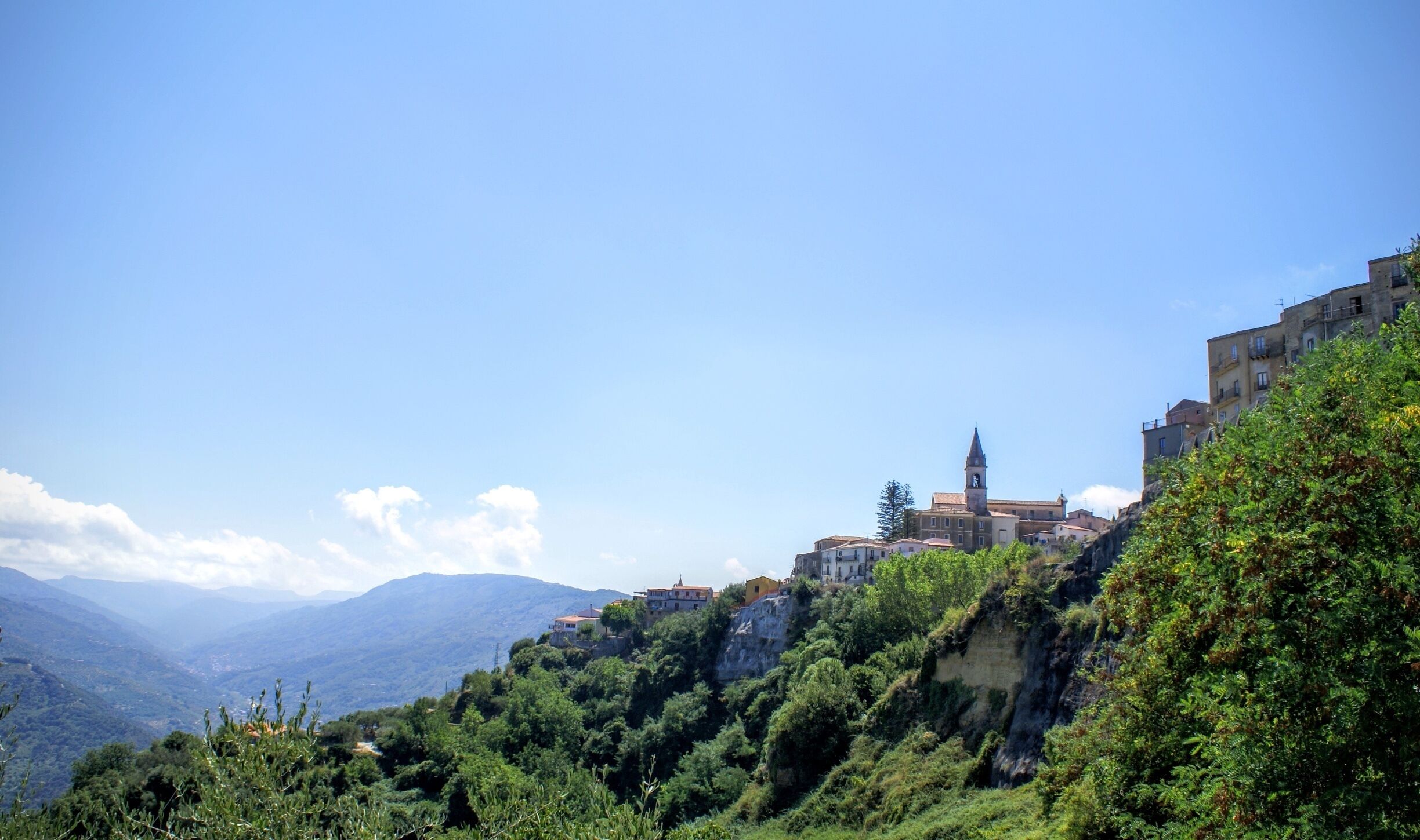 A mountainous landscape with a prominent church on a hill, surrounded by lush greenery and residential buildings.
