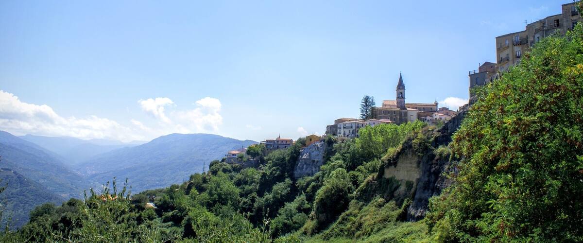 A mountainous landscape with a prominent church on a hill, surrounded by lush greenery and residential buildings.