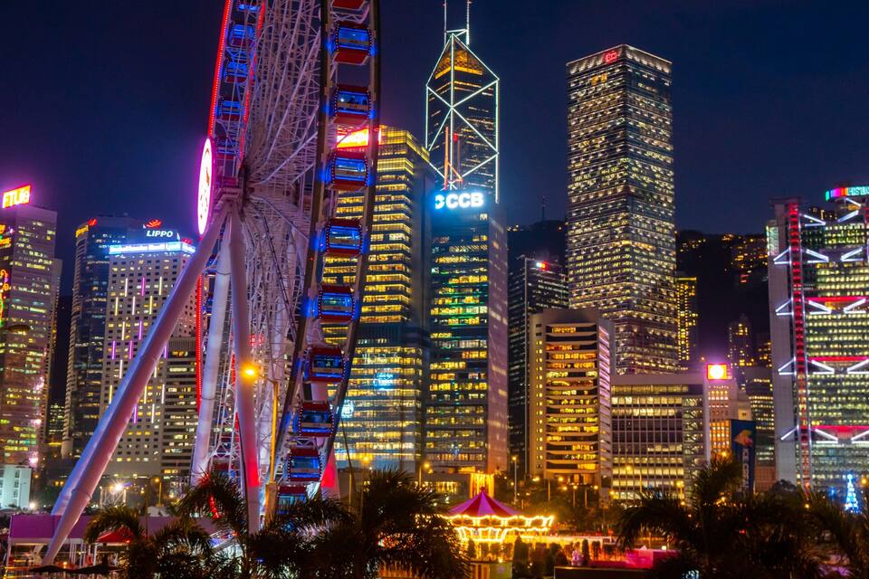 A cityscape at night with illuminated skyscrapers and a Ferris wheel.