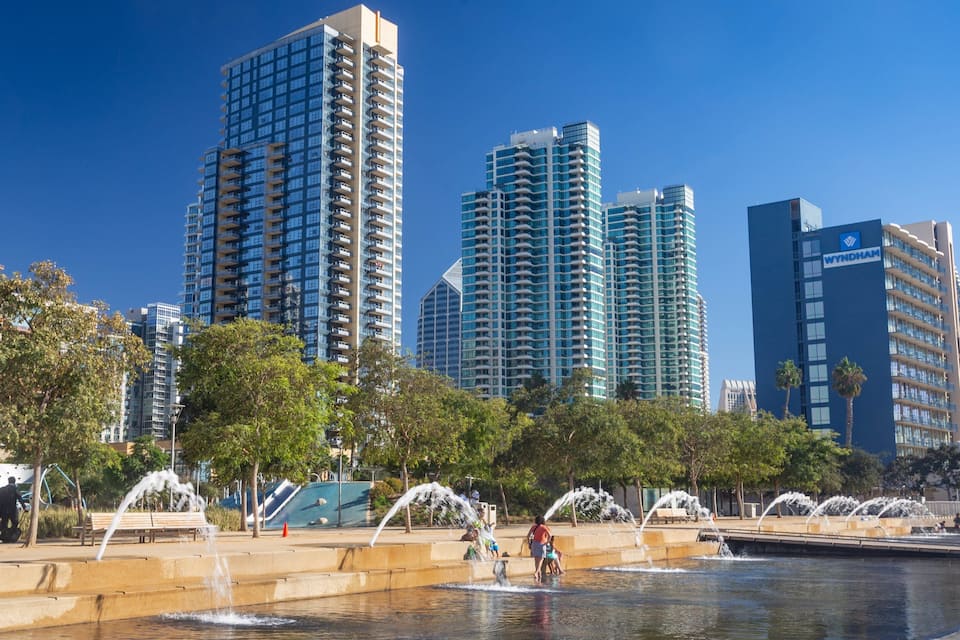 Eine Skyline mit modernen Hochhäusern, einem Brunnenbereich und Menschen, die den Park genießen.